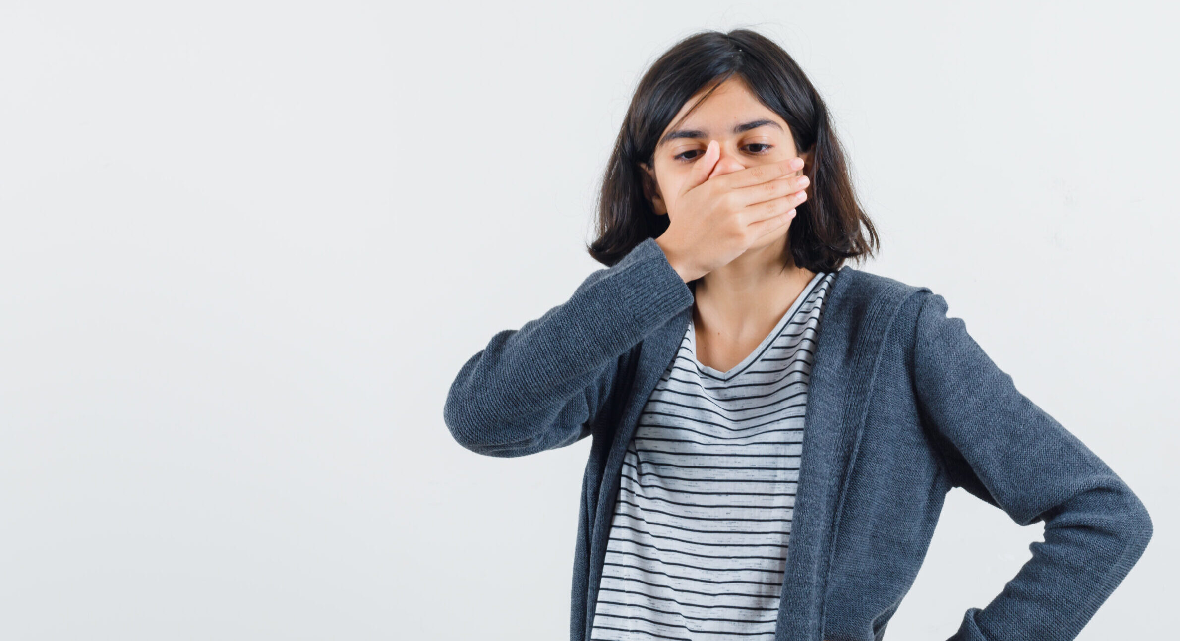 little girl holding hand on mouth in t-shirt, jacket and looking scared. front view.